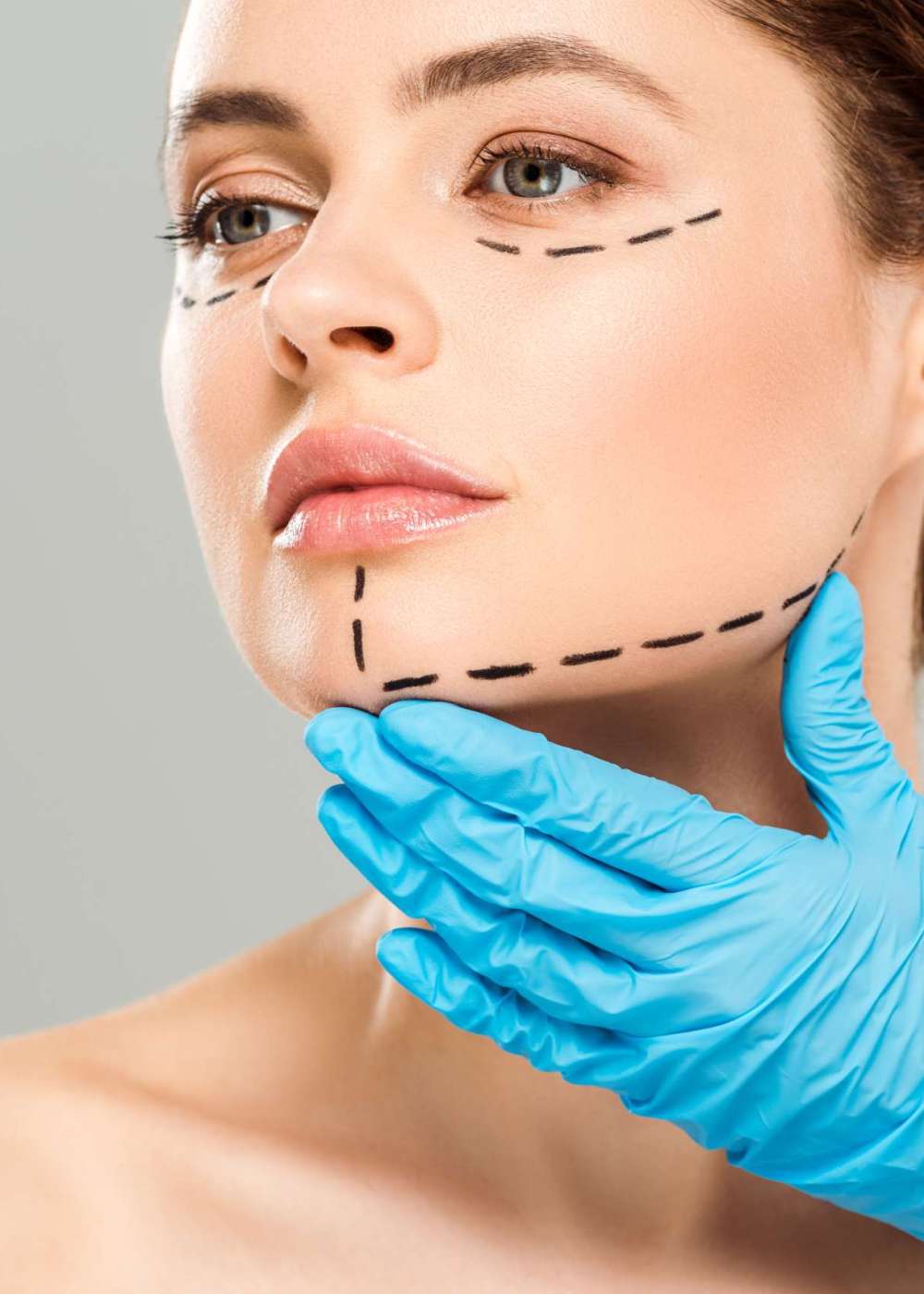 cropped view of plastic surgeon touching face of attractive woman with marked face isolated on grey